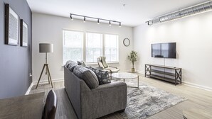 A modern living room with a grey sofa, a round coffee table, and a flat-screen TV. - Beautiful 1BR in Midtown and the Medical District  (Memphis)
