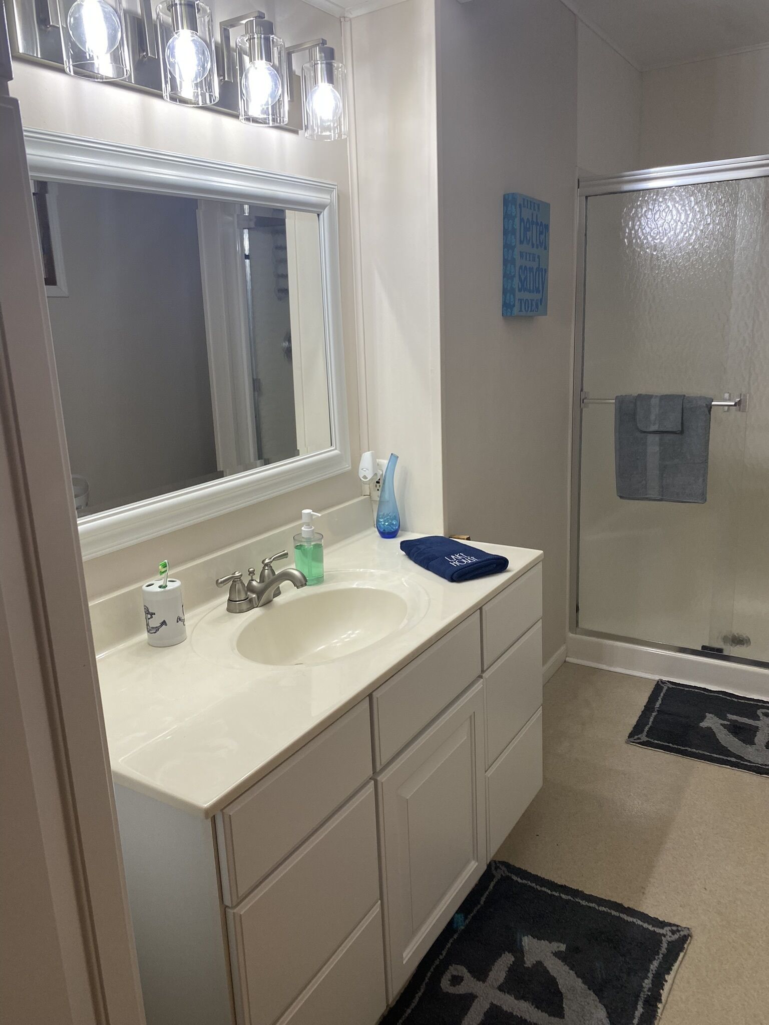 Un baño con un lavabo blanco, un espejo, un perchero para toallas y una puerta de ducha.