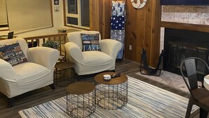 Una sala de estar acogedora con paredes de madera, dos sillones blancos, una chimenea y un televisor.