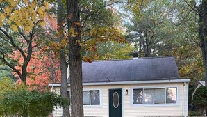 Una casa de un piso con techo oscuro y puerta verde, rodeada de césped con hojas de otoño dispersas.