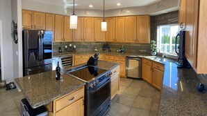 Una cucina moderna con piani di lavoro in granito, elettrodomestici in acciaio inossidabile, pensili in legno e illuminazione a sospensione.