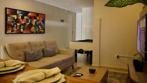 Una sala de estar con un sofá color beige, un cuadro en la pared, una mesa de billar y un televisor.