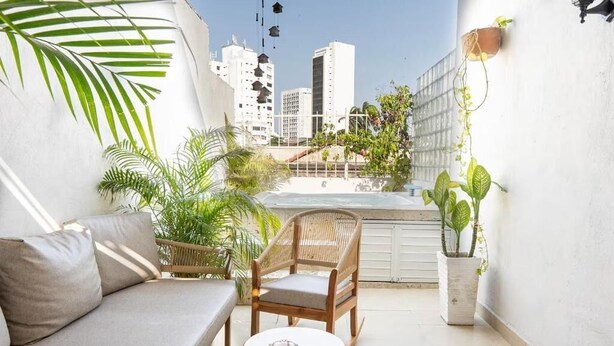 Un balcón con sofá, sillas de mimbre, una mesita y plantas en macetas.