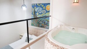 Un baño moderno con una bañera revestida de mosaicos, un cuadro de una escena de pueblo y una escalera con barandilla negra.