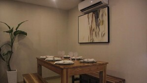 Un comedor con una mesa de madera dispuesta para cuatro personas, un banco y una planta en maceta.