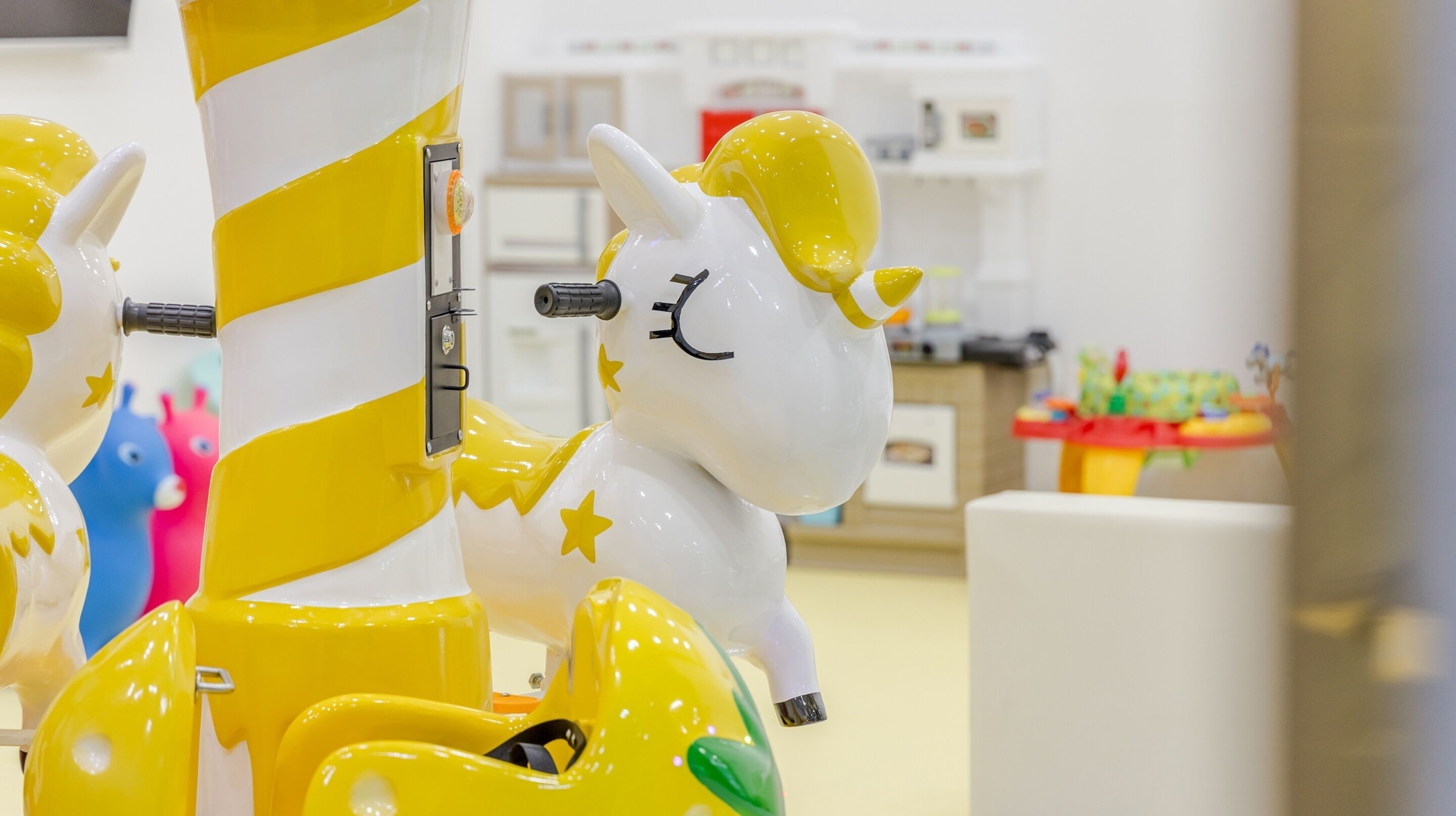 Un carrusel con caballos amarillos y blancos, incluyendo un unicornio, en un espacio interior bien iluminado.