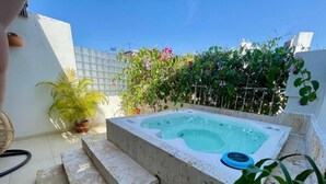 A hot tub in a backyard with steps leading up to it, surrounded by potted plants and a white wall.