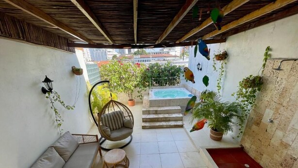 A cozy patio with a sofa, chairs, a small table, a hot tub, and potted plants.