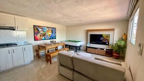 A modern living room with a sofa, a dining table, a TV, and a kitchen area.