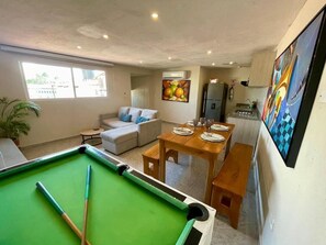 A pool table in a living area with a sofa and a dining table set for four.