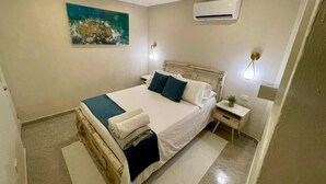 A bedroom with a bed, bedside tables, an air conditioner, and a wall-mounted artwork.