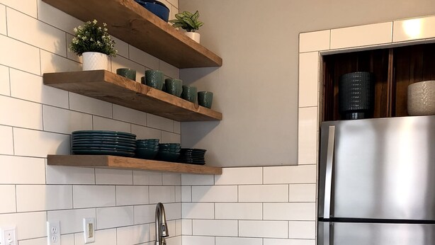 Una cocina moderna con armarios blancos, un refrigerador de acero inoxidable y estantes de madera con vajilla y plantas.