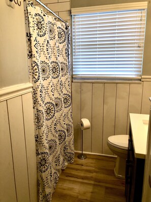 A bathroom with a shower curtain, toilet, and window with blinds.