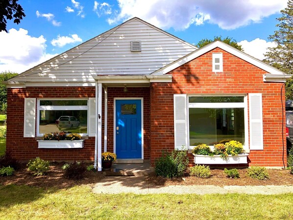 A small brick house with a blue door, white shutters, and a small porch area.