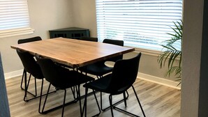 Un comedor con mesa de madera y sillas negras, una lámpara colgante y una ventana con persianas.