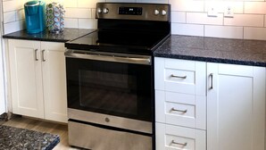 Una cocina con armarios blancos, un microondas negro, una estufa y una cafetera.