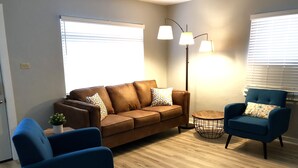 Una sala de estar con un sofá marrón, dos sillones azules, una mesita redonda y una lámpara de pie.