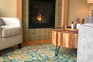 A cozy living room with a fireplace, a patterned rug, and a wooden coffee table.