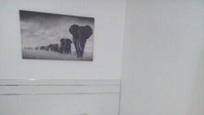 A small, single-bed room with a white mattress and a headboard. There is a wall-mounted picture above the bed. - Apartement Meublé à Loué aux Almadies (Dakar)