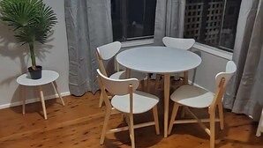 Une pièce avec une table ronde en bois et quatre chaises, une plante en pot et une fenêtre avec des rideaux.