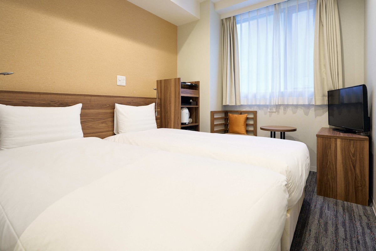 A hotel room with a large bed, a television on a wooden stand, a small table, and a window with curtains.