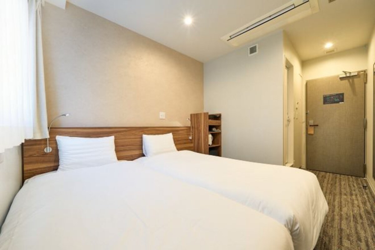 A hotel room with a large bed, a wooden headboard, a small wooden cabinet, and a door with a sign.