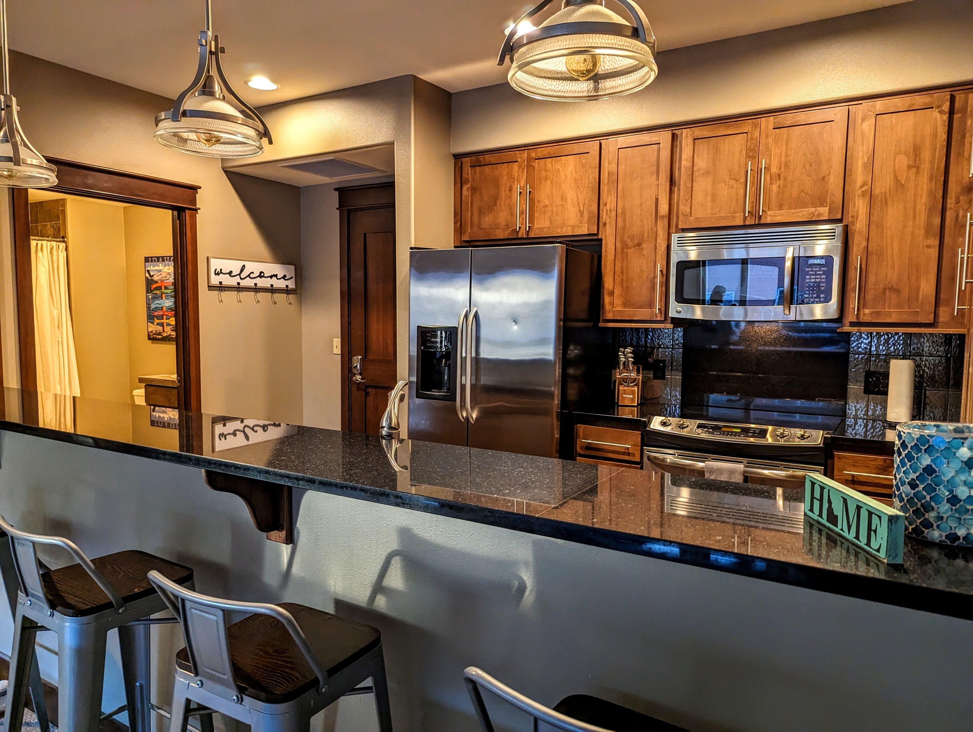 A modern kitchen with stainless steel appliances, wooden cabinets, and a bar area with stools.