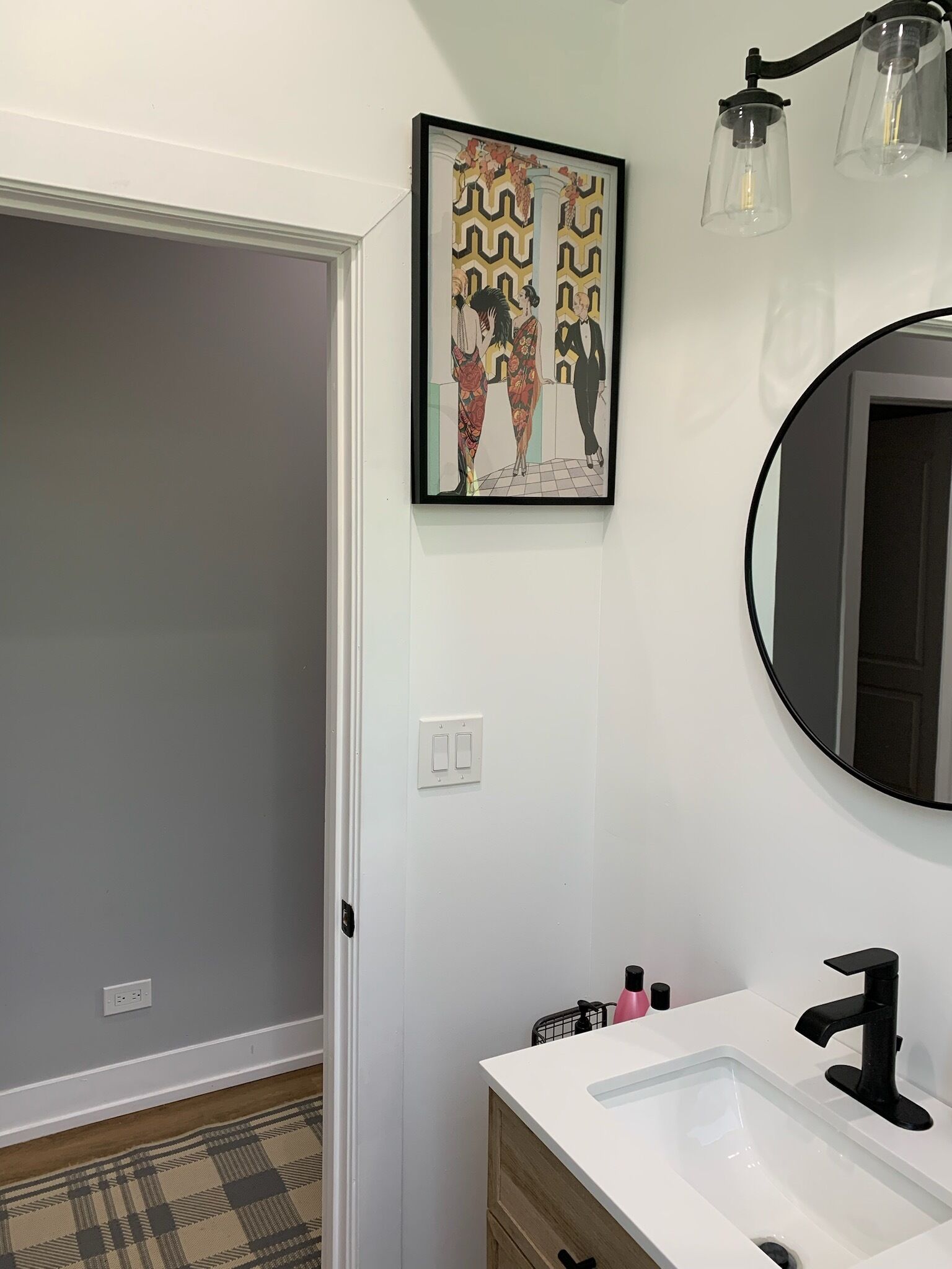 Un baño con lavamanos blanco, grifo negro y una obra de arte enmarcada sobre el espejo.