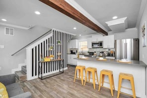 A modern kitchen with white cabinets, stainless steel appliances, and a wooden staircase.