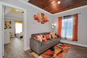Un salon avec un canapé gris, des rideaux orange et un tapis coloré.