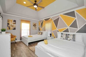 A modern bedroom with two beds, a ceiling fan, and geometric wall art.