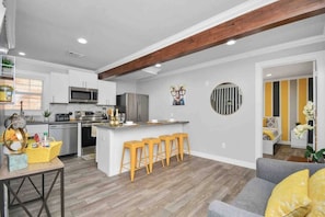 A modern kitchen with white cabinets, a central island with stools, a microwave, and a refrigerator.