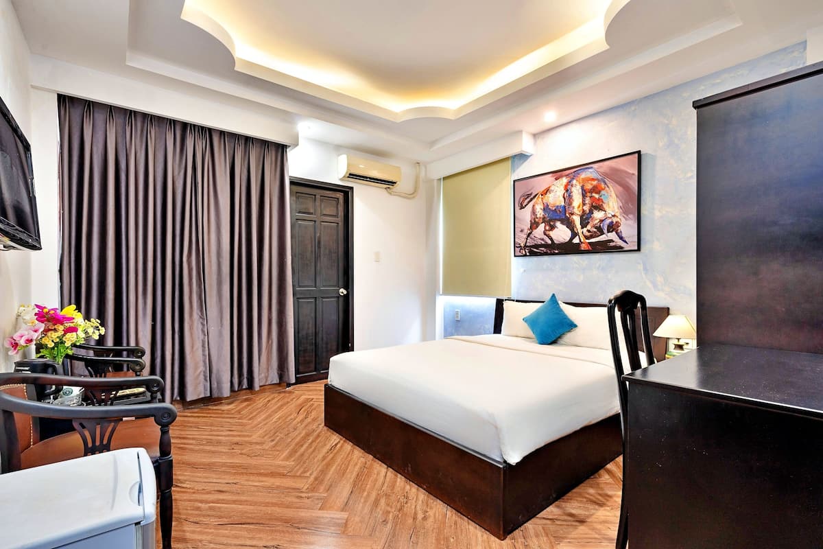 A hotel room with a large bed, a desk, a chair, a TV, and an air conditioning unit.