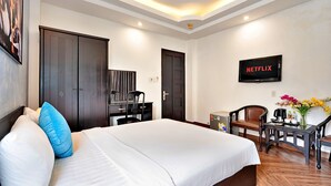 A hotel room with a large bed, a desk with a chair, a television displaying 'NETFLIX', and a small table with a vase of flowers. - S79 Residences Yaya Bui Vien (Ho Chi Minh City)