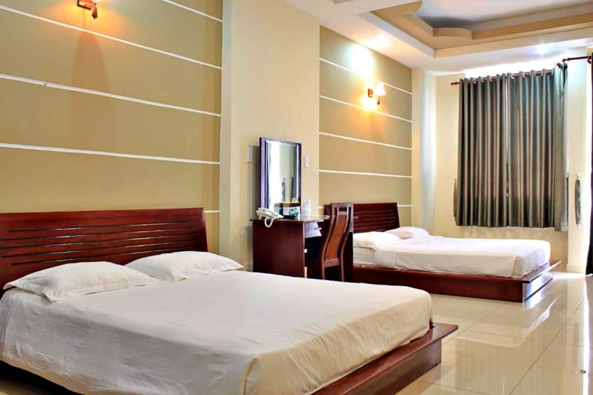 A hotel room with two beds, a desk with a telephone, and a mirror on the wall.