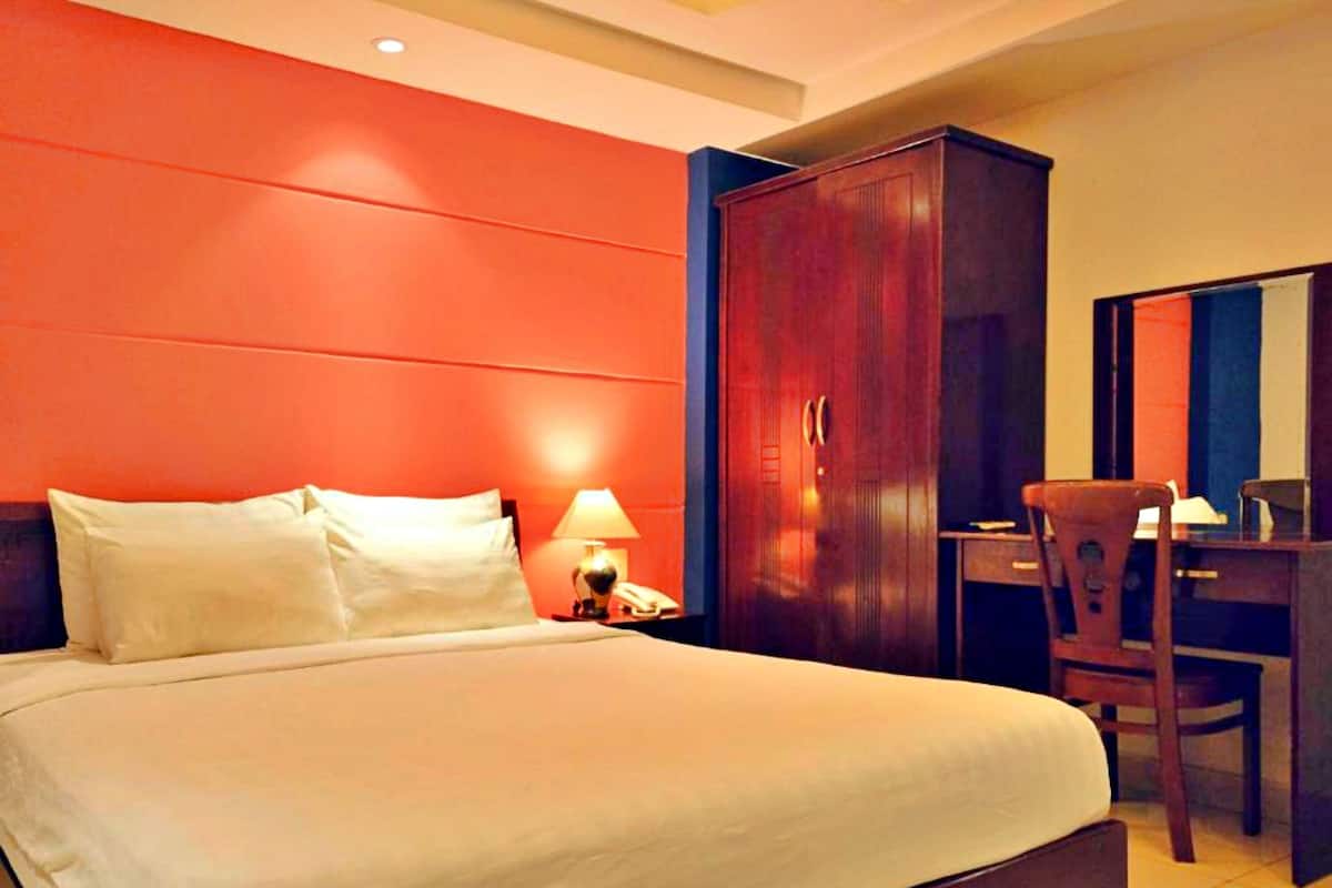 A hotel room with a large bed, a desk, and a wardrobe.