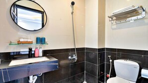 A modern bathroom with a black and white tiled wall, a round mirror, a glass shelf with toiletries, a white sink, a shower, and a toilet. - S79 Residences Yaya Bui Vien (Ho Chi Minh City)