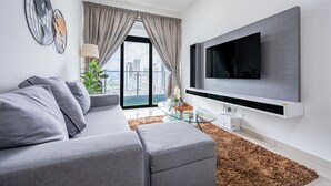 A modern living room with a grey sofa, a glass coffee table, and a mounted TV.