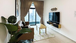 A modern living room with a large window, a sofa, a coffee table, and a flat-screen TV mounted on the wall.