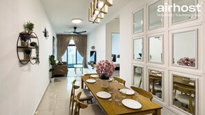 A hotel dining area with a long wooden table set for four, surrounded by chairs. There is a ceiling fan above the table, and a potted plant on the left side.