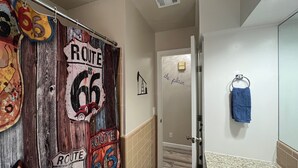 Un pasillo con una puerta de madera decorada con carteles de la Ruta 66, un tozaleta con una toalla azul y una puerta con un letrero que dice 'the plan'.