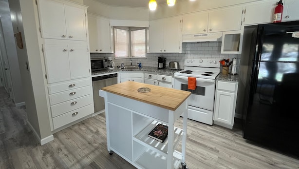 Una cocina moderna con armarios blancos, un refrigerador negro y una isla de madera.