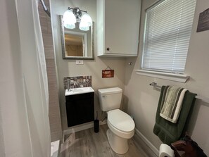 Une petite salle de bain avec des toilettes blanches, un lavabo doté d’un pare-éclaboussures à motifs, un miroir avec éclairage intégré et un porte-serviettes sur lequel est posée une serviette verte.