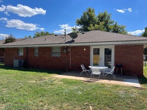 Une maison de plain-pied en briques, dotée d’un patio couvert, d’une antenne parabolique et d’une petite table avec des chaises.