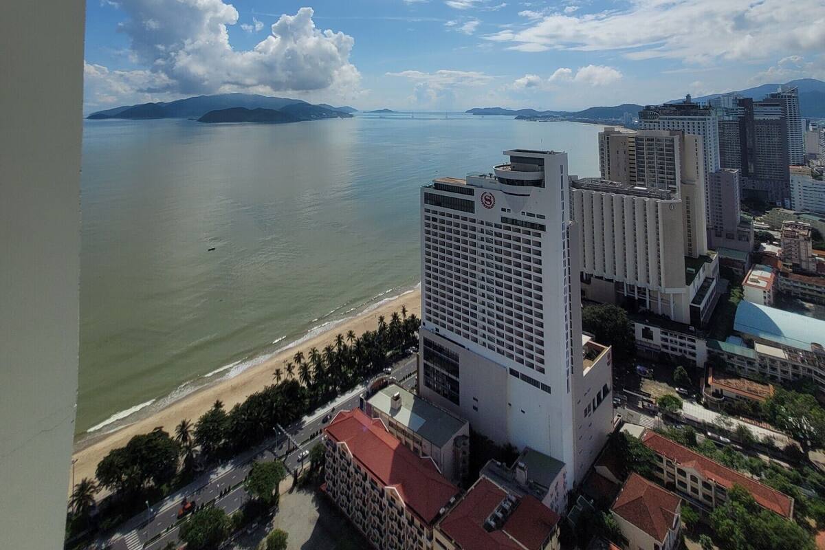 A coastal cityscape with a prominent hotel featuring a modern design, situated near a beach and a body of water.