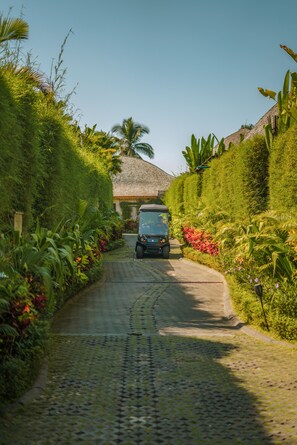 A paved pathway leading to a building with a thatched roof, surrounded by lush greenery and tropical plants. - Kanva Ubud (Tegallalang)