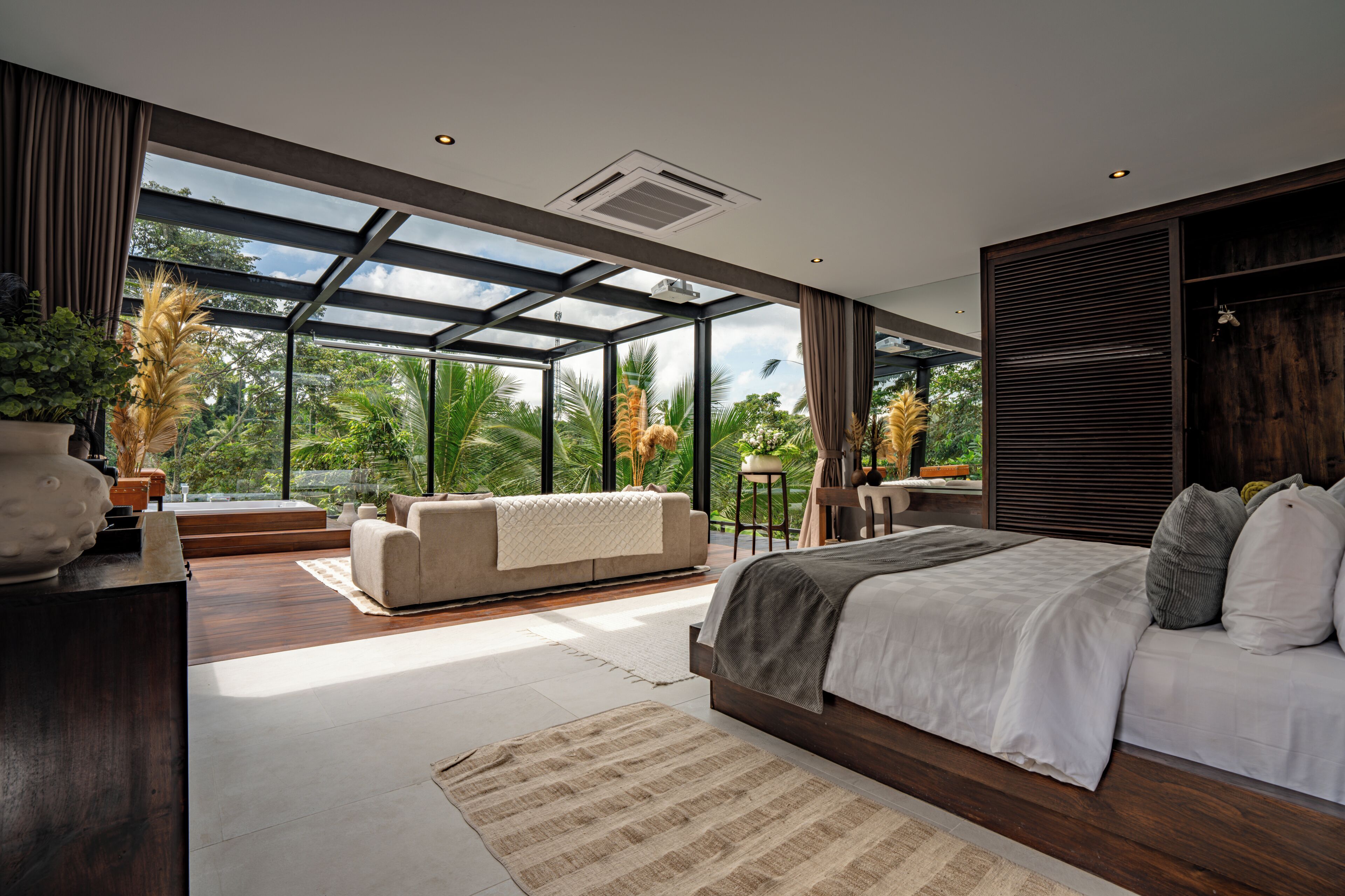 Un dormitorio moderno con una cama grande, un sofá y vistas a exuberante vegetación a través de amplios ventanales.