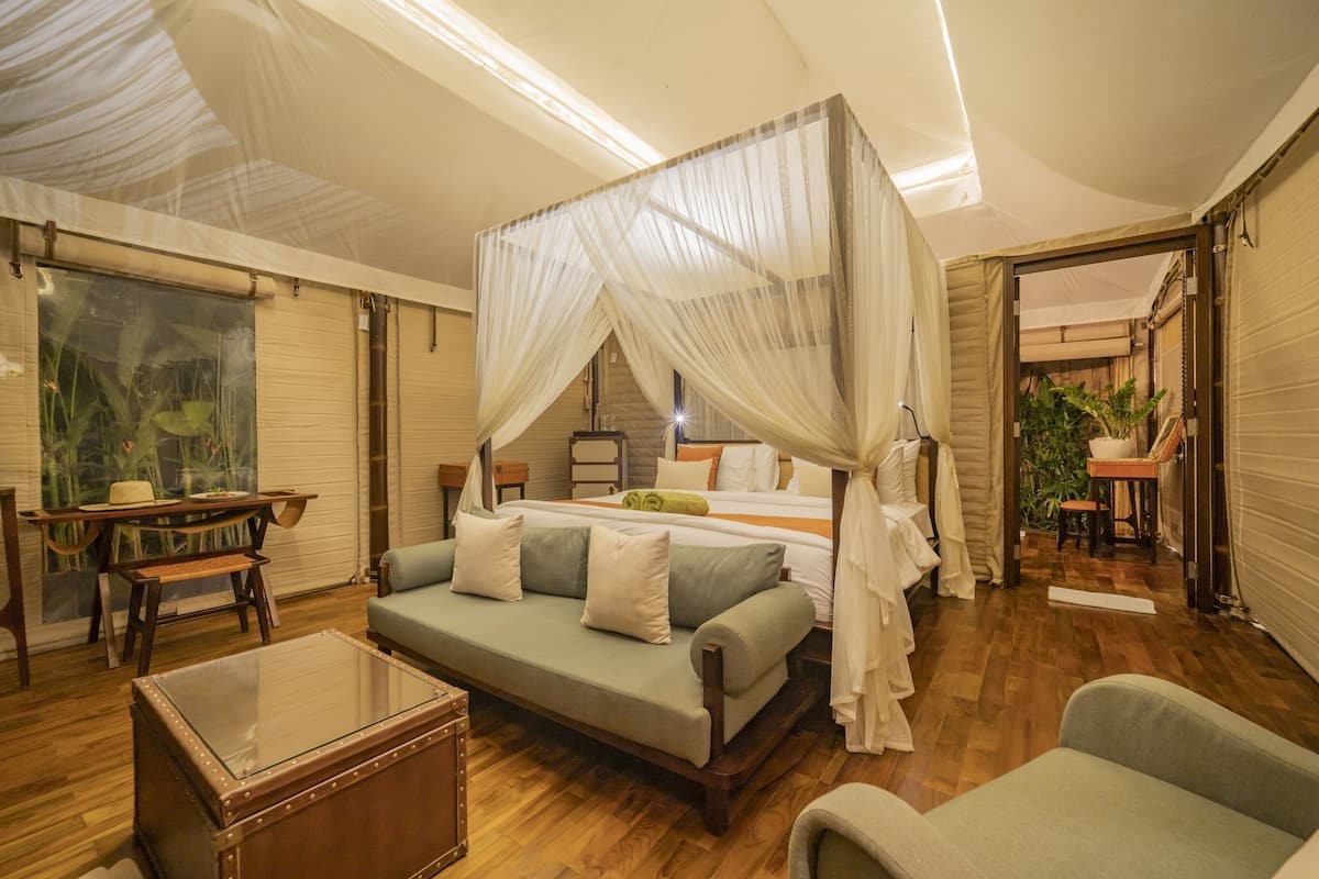A bedroom with a canopy bed, a sofa, a wooden coffee table, and a view of the outside.