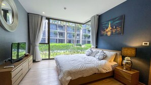 Une chambre moderne avec un grand lit, un téléviseur posé sur une commode et une vue sur la verdure.