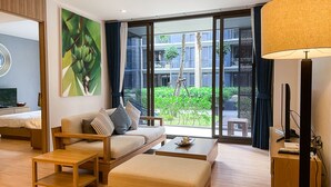 Une chambre d’hôtel moderne, dotée d’un canapé, d’une table basse, d’un téléviseur et d’une grande fenêtre donnant sur l’extérieur.